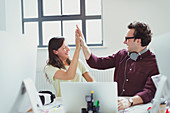 Computer programmers high-fiving at laptop in office