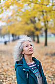 Thoughtful senior woman looking up at autumn trees in park
