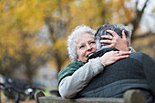 Affectionate senior couple hugging on bench in autumn park