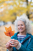 Senior woman holding orange autumn leaf in park