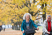 Carefree senior woman bike riding among trees in autumn park