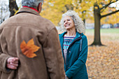 Senior husband surprising wife with autumn leaf in park