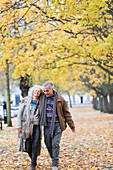 Senior couple walking among tress and leaves in autumn park