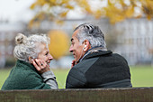 Senior couple sharing headphones, listening to music in park