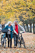 Senior couple walking bicycles among trees and leaves