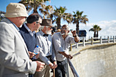 Active senior men tourist friends talking on sunny boardwalk