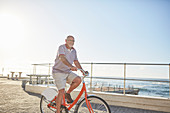 Senior man tourist bike riding on boardwalk along ocean