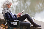 Active senior woman using digital tablet at park pond