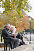 Couple using tablet, enjoying coffee and tea at autumn park