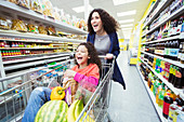 Playful mother pushing laughing daughter in shopping cart