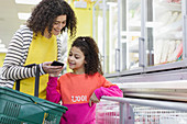 Mother and daughter with smart phone shopping in supermarket