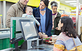 Friendly cashier helping couple with baby at supermarket