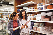 Happy women friends shopping for plates in home goods store