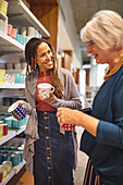Smiling worker helping senior woman shopping for mugs