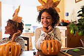 Happy girl in turkey hat carving pumpkin at table