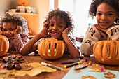 Portrait happy brother and sisters carving pumpkins at table