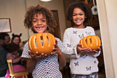 Portrait happy brother and sister holding carved pumpkins