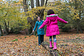 Mother and daughter balancing on fallen log in autumn woods