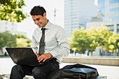 Smiling businessman working on laptop in urban park