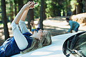 Woman taking self-portrait on hood of car in woods