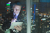 Businessman using digital tablet in urban window at night