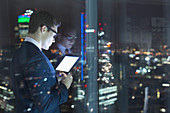 Businessman using digital tablet in urban window at night