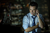 Businessman talking on cell phone in office at night