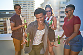 Carefree young friends drinking beer on sunny urban rooftop