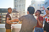 Carefree young friends dancing on sunny urban rooftop