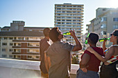 Young friends drinking beer on sunny urban rooftop