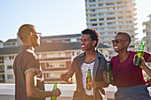 Friends talking and drinking beer on sunny rooftop balcony