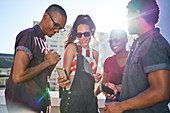 Young friends with smart phones on sunny rooftop balcony
