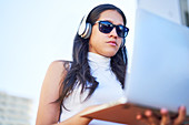 Young woman with headphones and sunglasses using laptop