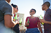 Happy young friends drinking beer on sunny rooftop balcony