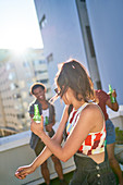 Young woman with beer dancing on sunny urban rooftop balcony