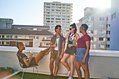 Young friends drinking beer on sunny urban rooftop balcony