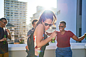Happy young friends dancing and drinking beer on rooftop