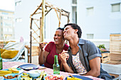 Happy young couple laughing and eating at patio table