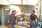 Happy young friends toasting beer over patio table