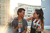 Happy young couple drinking beer on sunny rooftop balcony
