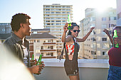Carefree young friends dancing on sunny rooftop balcony