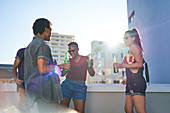 Friends dancing and drinking beer on sunny rooftop balcony