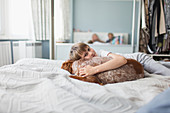 Portrait cute boy cuddling dog on bed