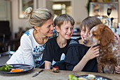 Happy mother and sons with dog at dinner table