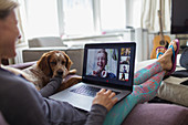 Woman video chatting with friends on sofa with dog