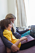 Mother and son with laptop video chatting on sofa