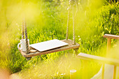 Laptop and coffee cup on swing in sunny garden