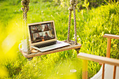 Colleagues video chatting on laptop on swing in garden