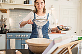 Teenage girl sifting flour for baking in kitchen