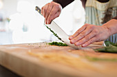 Woman cutting fresh herbs with knife on cutting board